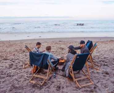 three men and one woman sitting on beach lounge in front fire pit near seashore