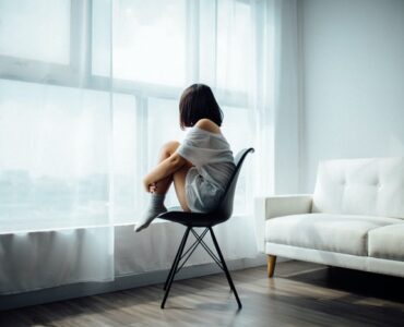 woman sitting on black chair in front of glass-panel window with white curtains